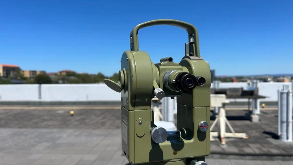 A green surveying theodolite on a rooftop under a clear blue sky