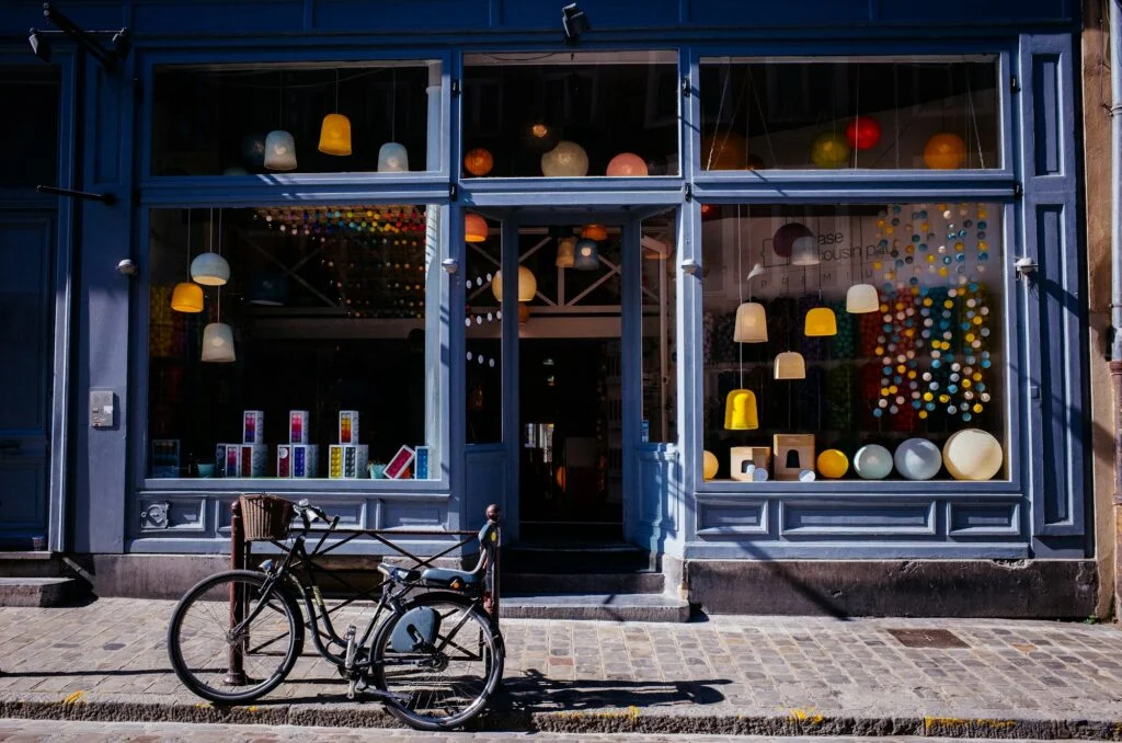 A bicycle parked on a cobblestone pavement outside a small lamp shop with a blue shopfront